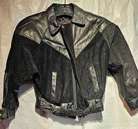 Front view of black leather-suede jacket on hanger showing belt and pockets