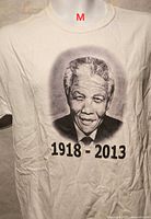 Front view of white T-shirt showing Mandela portrait and 1918-2013 text, size M tag location