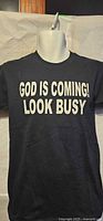 Front view of black T-shirt with white text "GOD IS COMING! LOOK BUSY" displayed on mannequin torso.