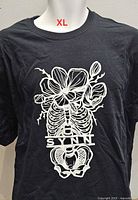 Front view of black men’s XL T-shirt displaying white skeleton floral SYNN graphic