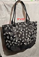Front view of tote bag hanging, showing skeletal hand print and handles