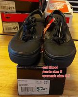 Pair of black Vans Old Skool sneakers on box showing size tag attached