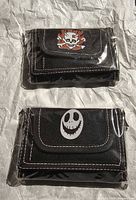 Two packaged black nylon wallets with skull and clown graphics