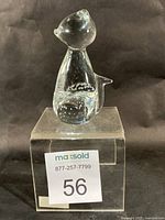 Full view of clear glass cat paperweight on acrylic riser