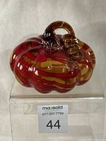 Front view of hand-blown glass pumpkin showing red and yellow swirls and coiled stem