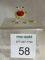 Front view of clear and green glass frog with red mouth on display block