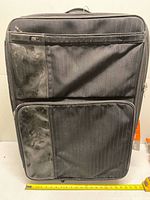 Front view of large black suitcase with two front pockets and tape measure indicating size