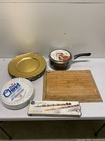 Lot overview showing chargers, saucepan, cutting boards, Royal Chinet pack, boxed olive tray set