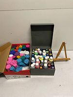 Lot overview showing box of craft sticks, metal box of paints, and tabletop easel
