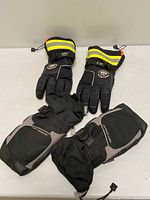 Both pairs of gloves displayed—Helly Hansen pair with hi-vis stripes above, Hot Paws pair below.
