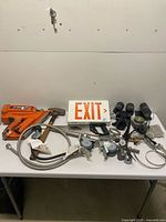 Overall lot on table including nail gun, hammer, EXIT sign, saw, casters and hoses