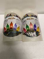 Front view of both light sets in clear plastic cylindrical boxes showing multicolor bulbs and labels