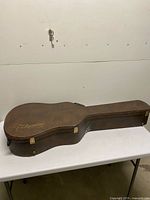 Closed brown Takamine hard shell guitar case on table