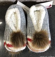 Top view of grey knit slipper socks with faux fur pom-poms and tags