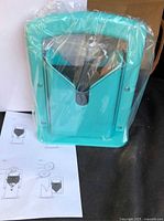 Teal bagel slicer in plastic wrap with instruction sheet