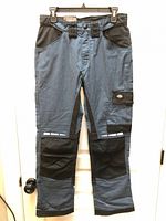 Full front view of blue Dickies work pants with black reinforced panels and tags attached