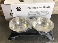 Elevated pet bowls in protective wrap beside original box