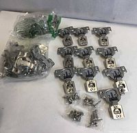 Bag of unused concealed hinges and screws plus eleven loose hinges laid out