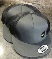 Two grey front, black mesh snapback caps side by side