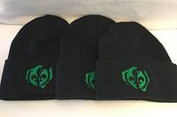 Three identical black beanies with green emblem displayed side by side