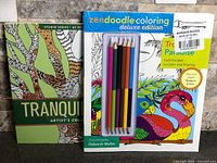Front covers of both colouring books; Zendoodle book shows attached coloured pencils