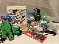 Group shot of all new items including LEGO polybag, origami kit, plush iguana, water bottle, erasers, robot toy, scissors, ball