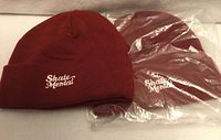 Two burgundy Skate Mental beanies, one in plastic, logo visible