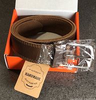 Belt coiled in orange box with buckle wrapped and handmade tag visible
