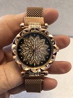 Front view of rose gold tone wristwatch showing rhinestone floral dial and bezel