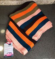 Full view of folded infinity scarf showing multicolour stripes and attached retail tag