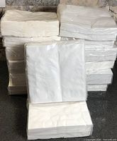 Stack of 14 sealed packs of white embossed napkins