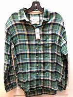 Front view of green/navy plaid flannel shirt on hanger with tag