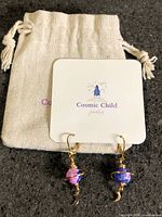 Full view of earrings on branded card with pouch