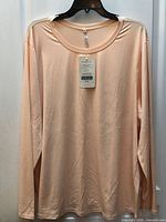 Front view of peach long sleeve top on hanger with tag attached