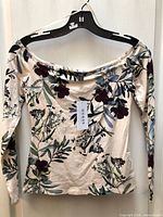 Front view of Guess floral off-shoulder top on hanger with tag attached