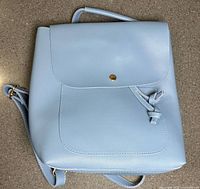 Front view of light blue backpack purse showing flap, pocket, and gold button