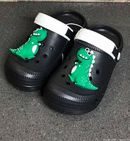 Top view of both clogs showing dinosaur charms and strap branding