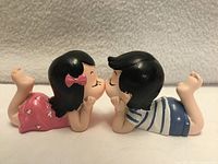 Girl and boy figurines joined at magnetized lips, side view