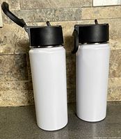 Two white stainless steel bottles standing upright against stone backsplash