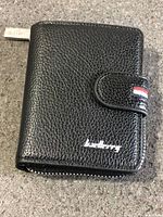 Front view of black Baellerry wallet showing pebble texture, snap tab with tri-colour accent, white logo