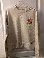 Front view of cream Woods floral crewneck showing left-chest graphic and overall condition