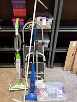 Wide view of steam mop, stick vacuum, step stool, dustpan, pole and bins on shelving