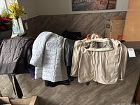 Four coats draped over counter: dark brown quilted, light grey puffer, dark green, beige hooded