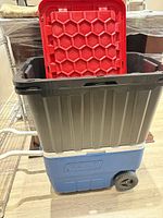 Side view showing tote stacked in cooler; wheels and Coleman logo visible