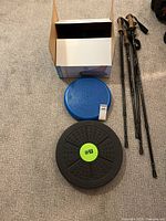 Overview of all items: MotionCiser box, blue cushion, black balance board, walking poles