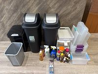 Full lot view showing two tall trash cans, smaller bins, storage boxes, and cleaning products