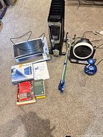 All items laid out on carpet: heater, fan, reacher, lamp, Blu-ray player, metal stand piece, manuals
