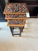 Stacked view of the three nesting tables showing carved tops and colour detail