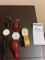 All three watches laid out: rectangular gold-tone with expansion band, round Geneva with red strap, round gold-tone with black strap