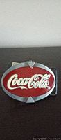 Front view of oval Coca-Cola belt buckle showing red center and silver border